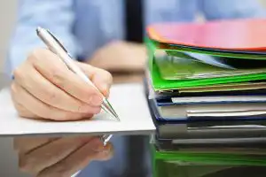 image of hand writing notes on pad with folders in foreground