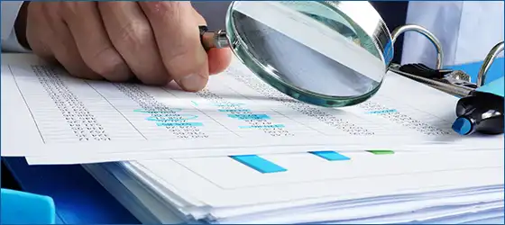 image of a hand using a magnifying glass to analyze reports